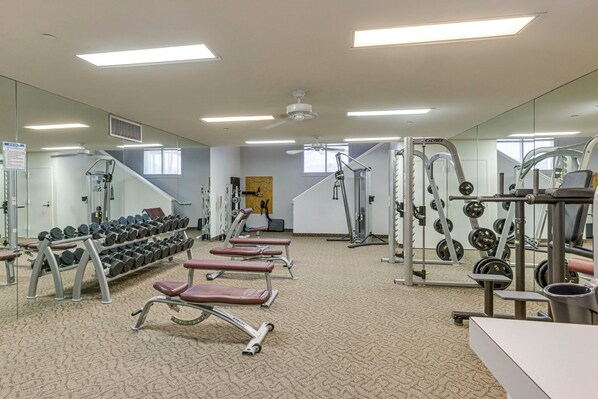 Un gimnasio con equipamiento de ejercicio, estantes para pesas y bancos.