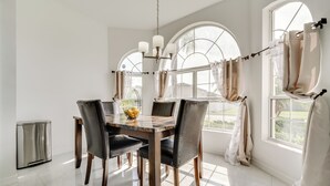 Ein Essbereich mit einem Marmortisch, vier Stühlen, einer Chandelierleuchtre und großen Fenstern mit Vorhängen.