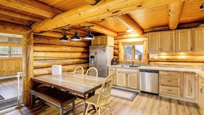 Ein Holzblockhaus-Innenraum mit einem Holzessttisch, Stühlen, einem Kühlschrank, einer Spüle und Holzschränken.