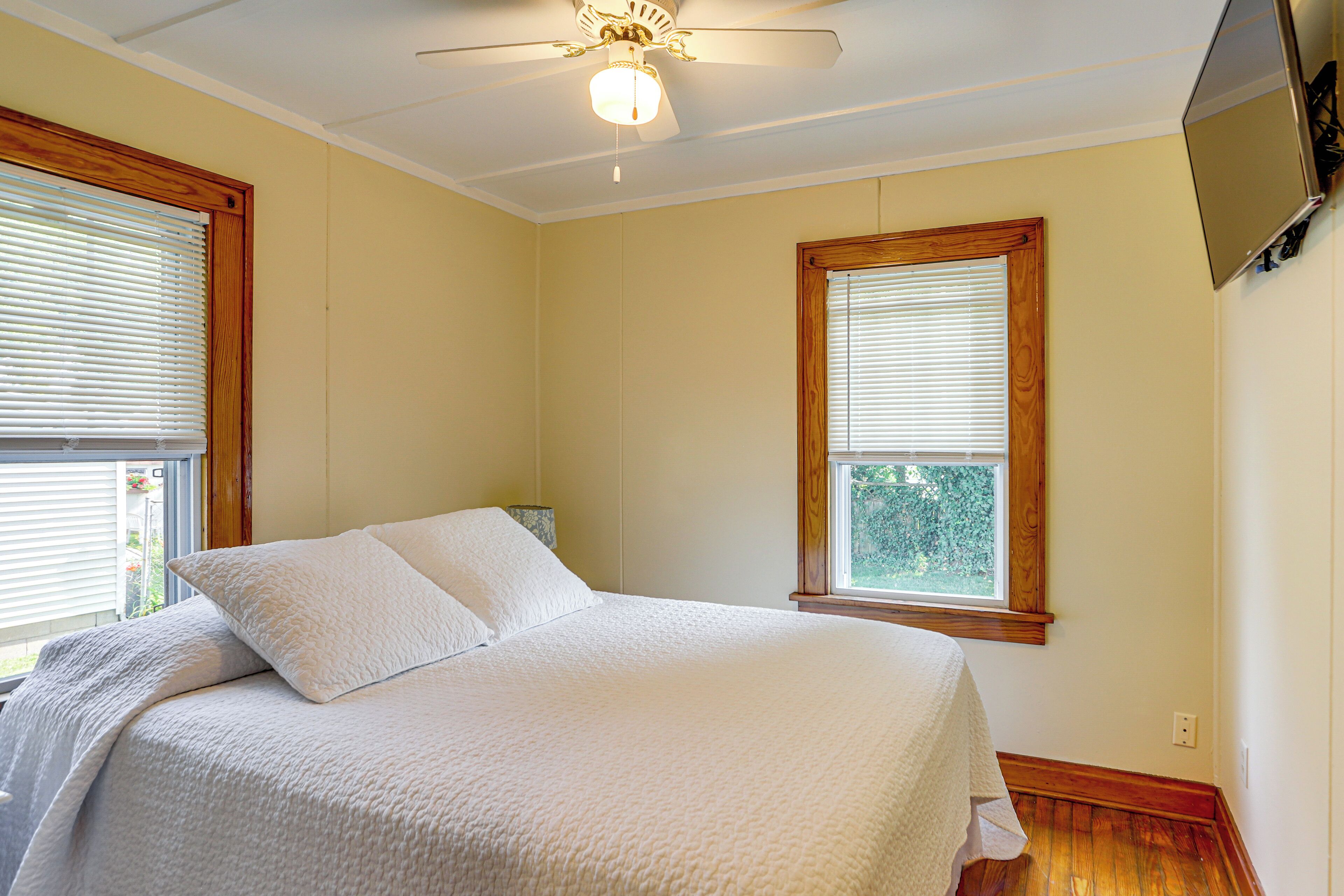 Ein Schlafzimmer mit einem Bett, einem Deckenventilator und zwei Fenstern.