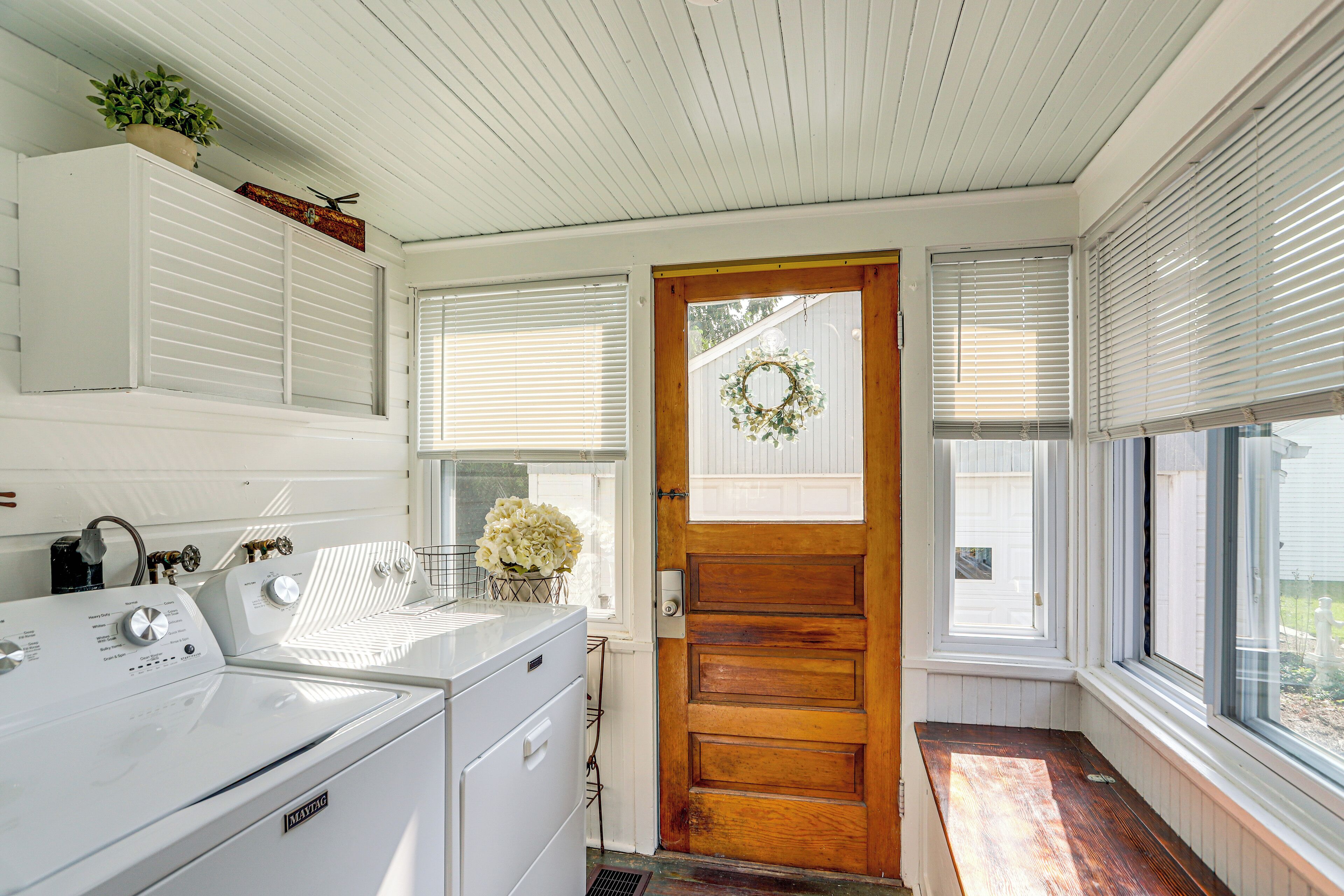 A laundry room with a washer and dryer, wooden door, and windows with blinds.