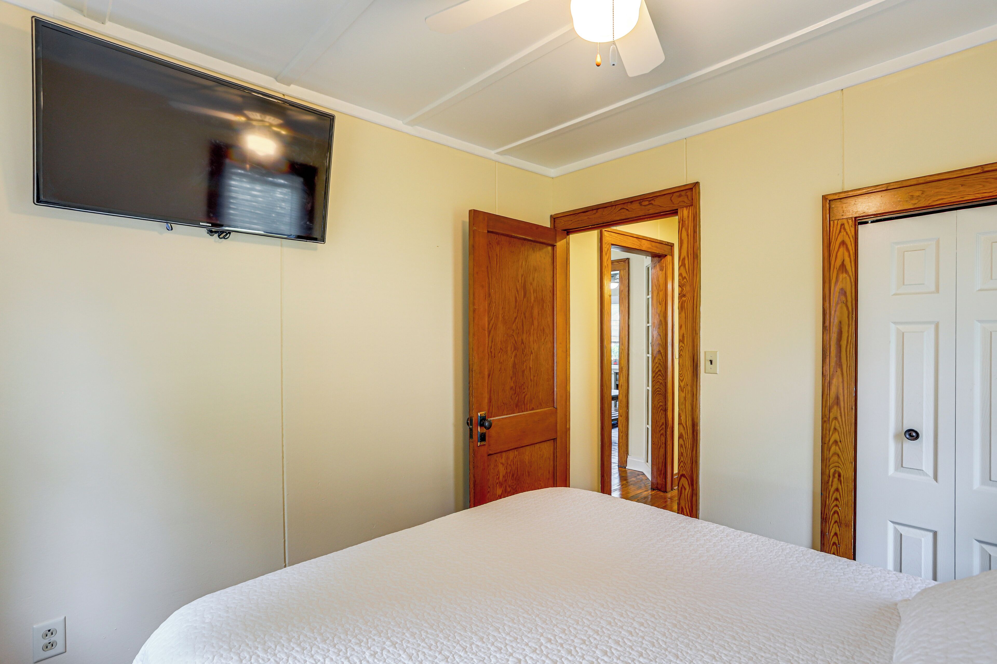 Une chambre à coucher avec un lit, un téléviseur fixé au mur et une porte donnant sur une autre pièce.