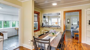 A dining area with a wooden table, chairs, and a vase of flowers. There is a window with blinds and a door leading to another room. - Walk to Private Beach: Lake Erie Retreat w/ Yard! (Huron)