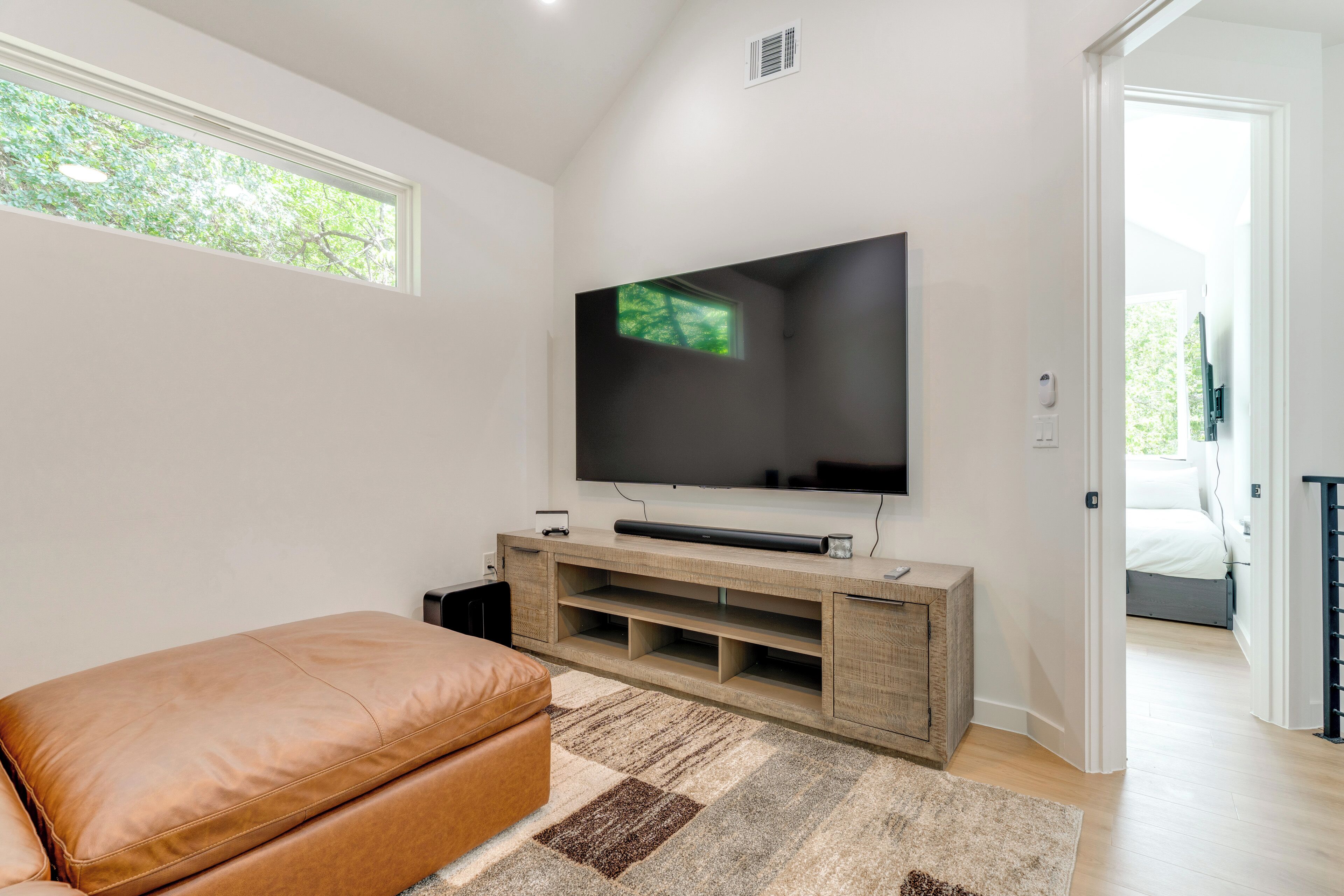 Ein modernes Wohnzimmer mit einem großen Flachbildfernseher an einer Holz-Unterhaltungsecke, einem braunen Ledersofa und einem gemusterten Teppich.
