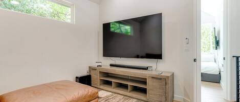Ein modernes Wohnzimmer mit einem großen Flachbildfernseher an einer Holz-Unterhaltungsecke, einem braunen Ledersofa und einem gemusterten Teppich.