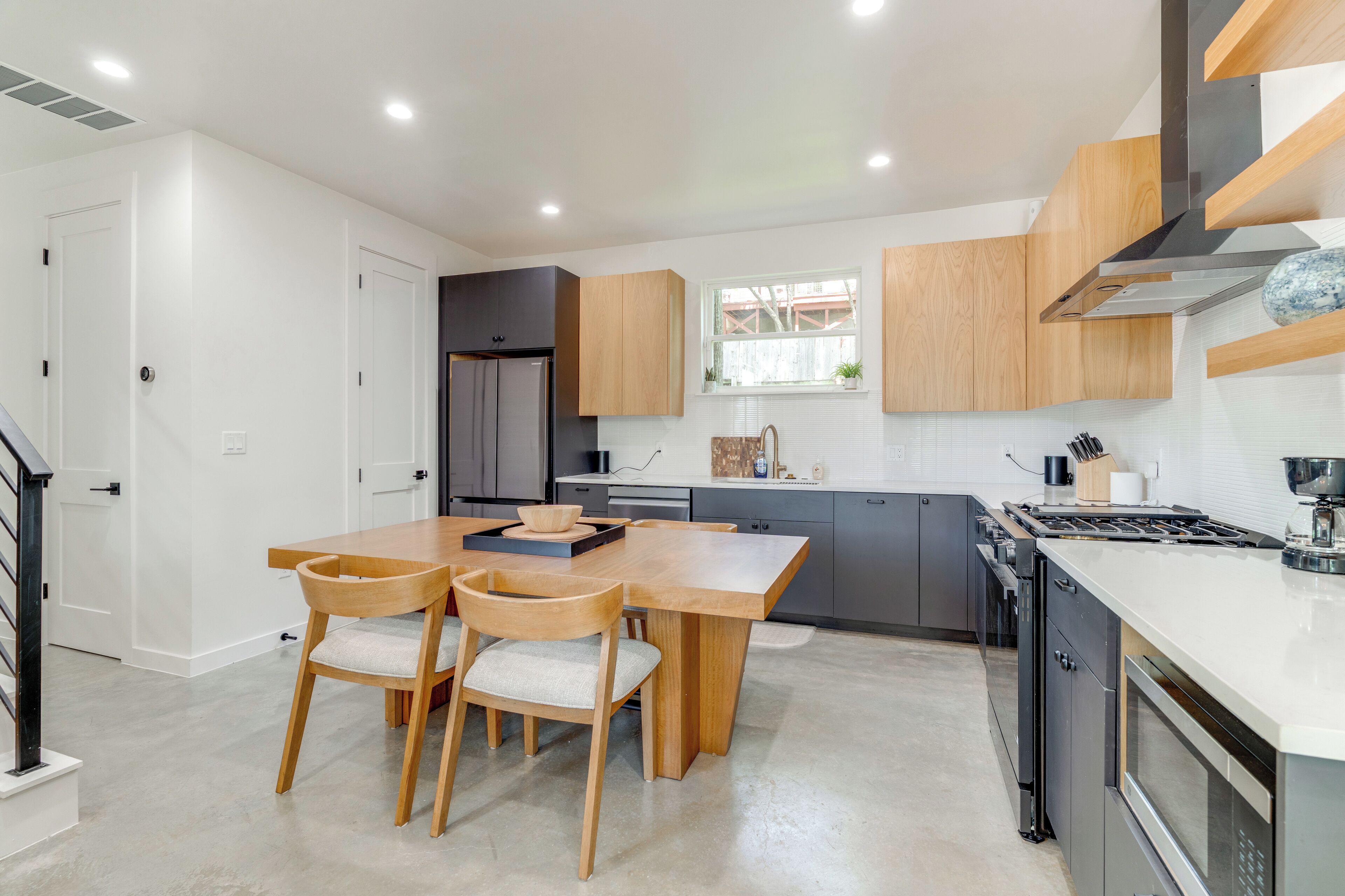 A modern kitchen with a wooden dining table and chairs, a built-in stove, and grey cabinets.