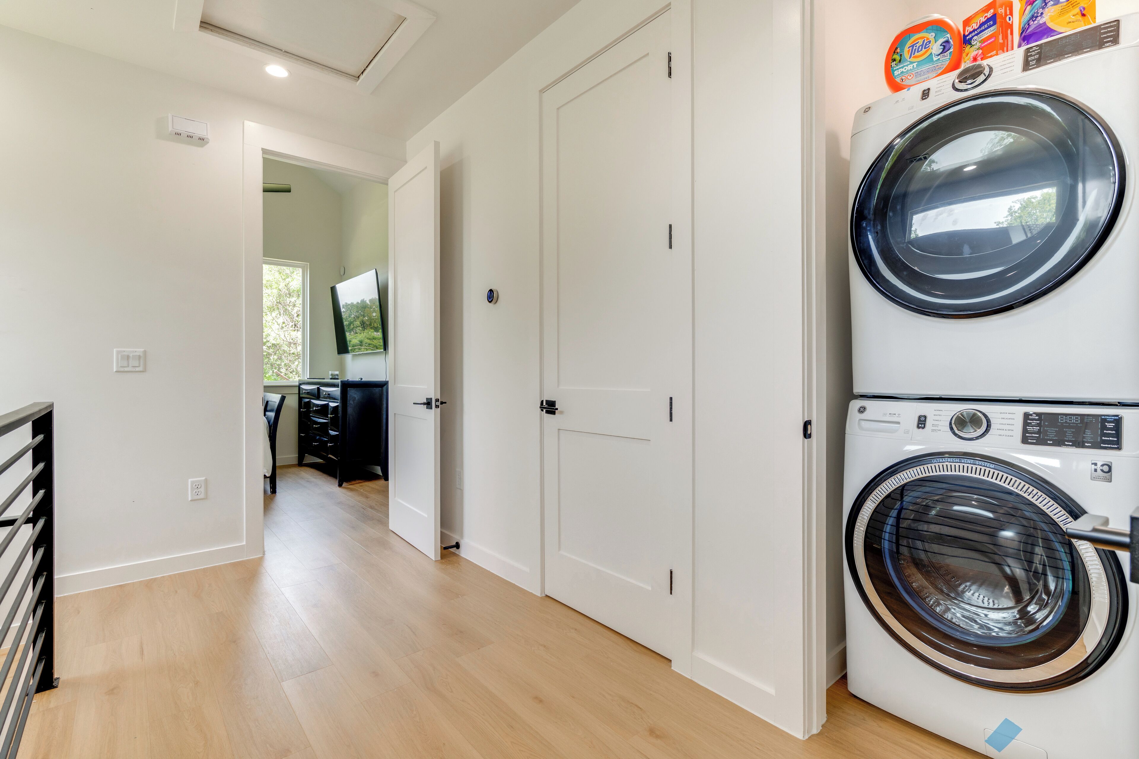 A laundry area with a front-loading washer and dryer, a door leading to another room, and a visible power outlet on the wall.