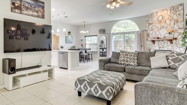A modern living room with a flat-screen TV, a sofa, an ottoman, and a stone accent wall. - Jacksonville Family Home: Near Shopping & Dining! (Jacksonville)