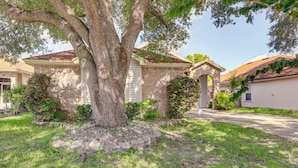 A residential house with a large tree in the front yard, a brick exterior, and a driveway leading to the garage. - Jacksonville Family Home: Near Shopping & Dining! (Jacksonville)