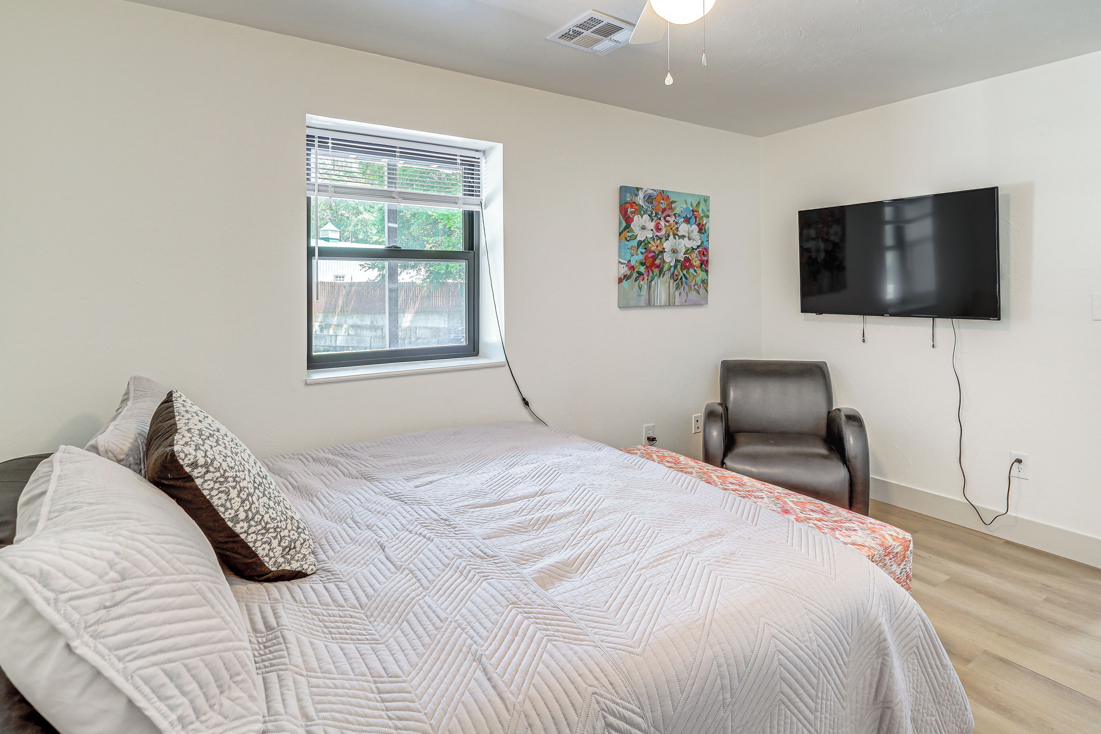 A bedroom with a bed, a chair, a TV, and a window.