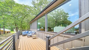 A wooden deck with outdoor seating, large windows, and a view of trees. - Family Fun! Lake Eufaula Home w/ Wraparound Deck (Eufaula)