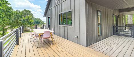 A wooden deck with a table and chairs, a railing, and a building with large windows.