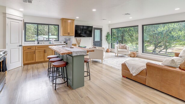 A modern kitchen with a central island, bar stools, and a large window overlooking greenery. - Family Fun! Lake Eufaula Home w/ Wraparound Deck (Eufaula)