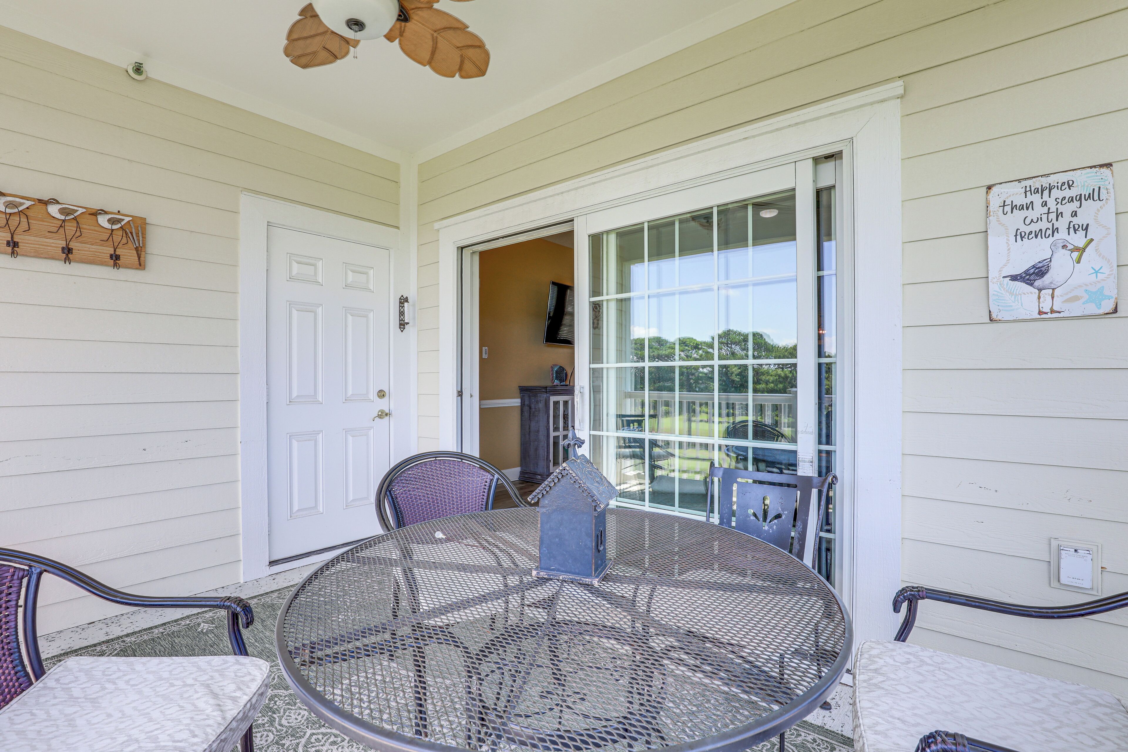 Un patio couvert avec une table et des chaises rondes en métal, une porte blanche et une vue à travers une porte vitrée.