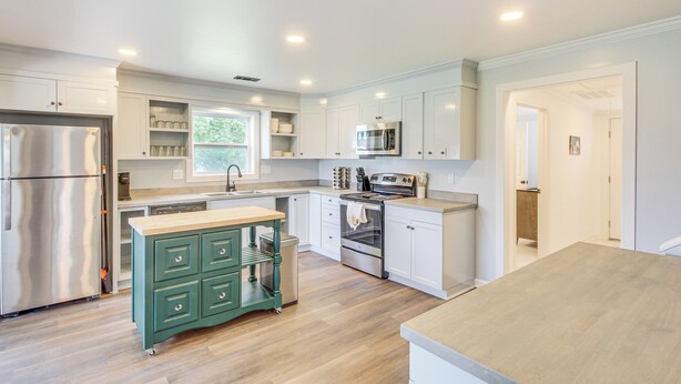 A modern kitchen with white cabinets, stainless steel appliances, and a green rolling cart. - Walk to Winery! Home w/ Patio & Yard in Holt (Holt)