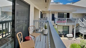 A balcony with wicker chairs and a small table, overlooking a residential area with a white building and a staircase. - Endless Summer #A30 | Close to Beach + 2 Pools (Panama City Beach)