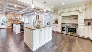 A spacious kitchen with a large island, white cabinetry, a brick accent wall, and a stone backsplash. - 7,100 Sq Ft Retreat w/ Gazebo + Koi Pond in Wayne! (Wayne)