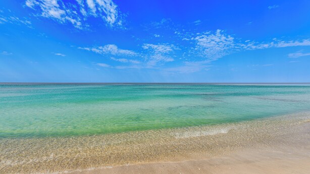 Ein Strand mit klarem, türkisblauem Wasser und einem sandigen Ufer unter einem strahlend blauen Himmel.