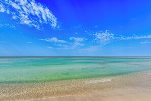 Una playa con agua turquesa cristalina y una orilla arenosa bajo un cielo azul brillante.
