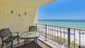 Ein Balkon mit Tisch und Stühlen mit Blick auf einen Strand, der mit Sonnenschirmen und Liegestühlen ausgestattet ist.