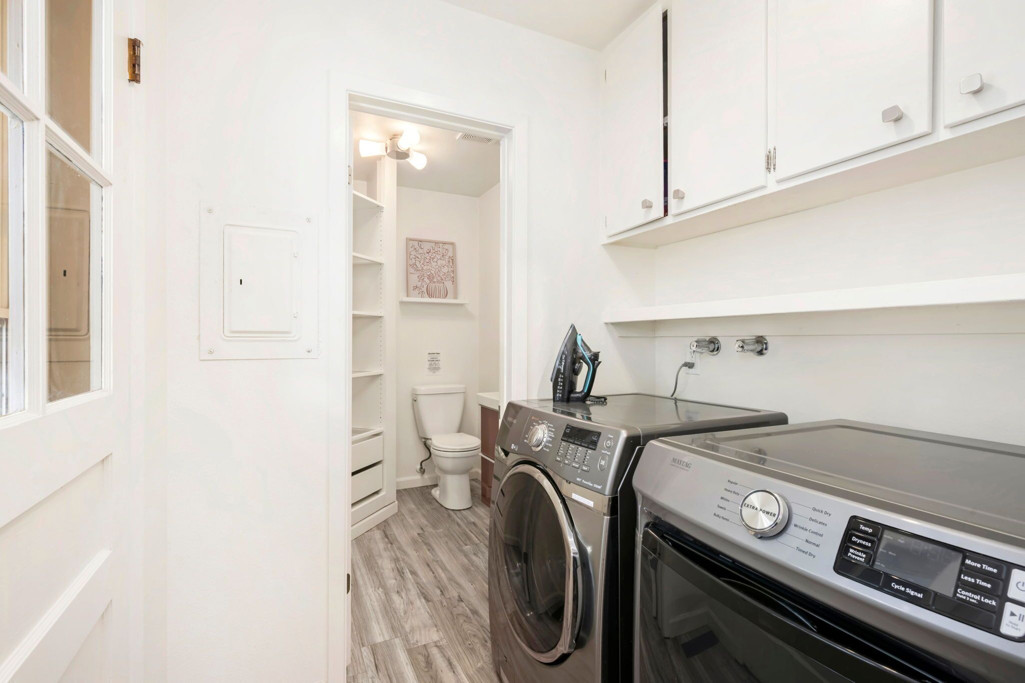A laundry room with a front-loading washing machine, a dryer, and a shelving unit above the dryer.