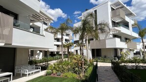 A modern multi-story residential building with balconies, a central courtyard with palm trees, and a paved walkway. - Santa Rosalia Mar Y Sol - App at the lake (MC)