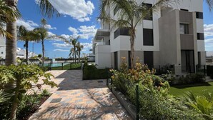 A modern building with a flat roof, large windows, and a paved walkway with palm trees. - Santa Rosalia Mar Y Sol - App at the lake (MC)