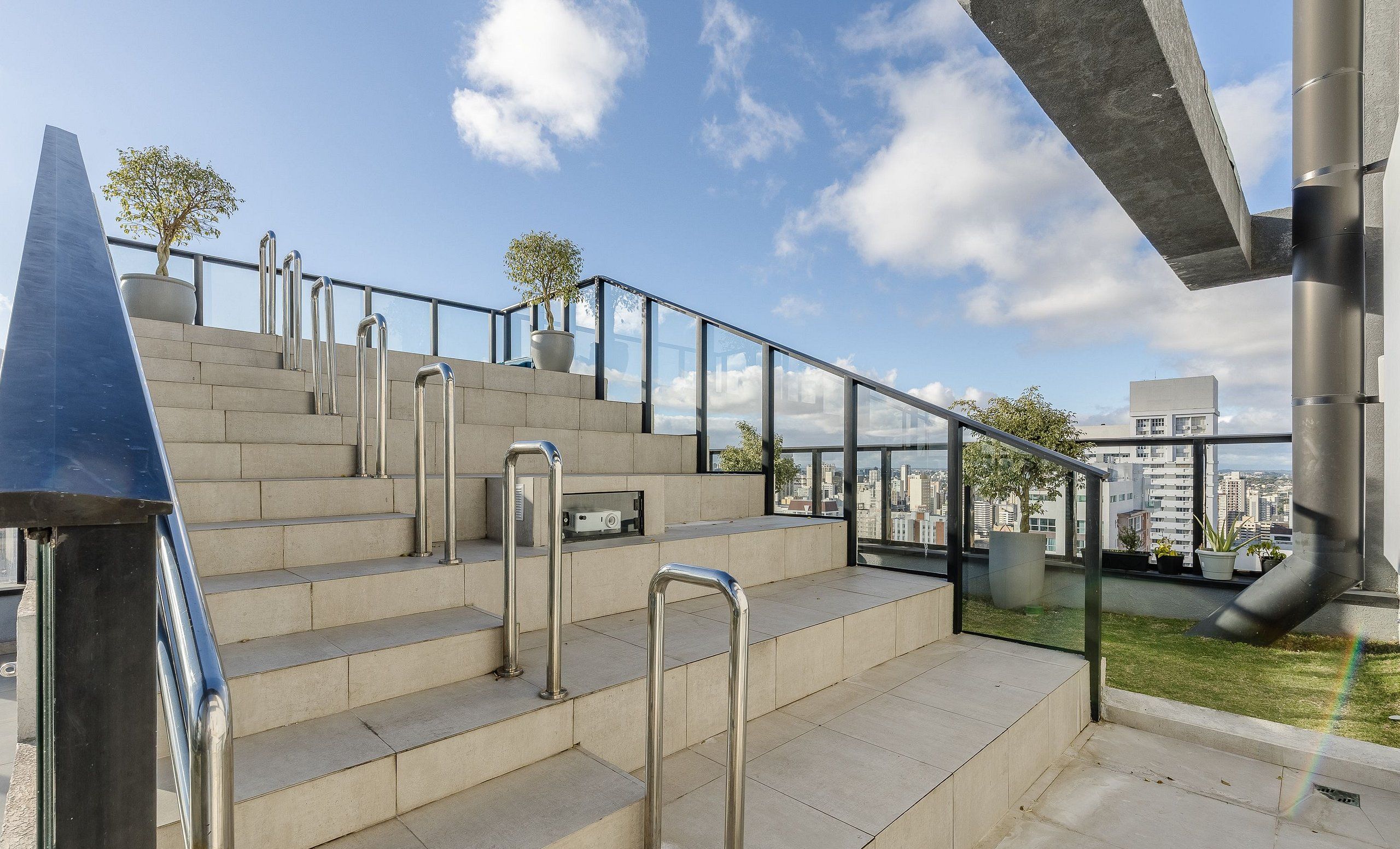 A modern outdoor staircase with metal railings, leading to a glass balcony with a city view.