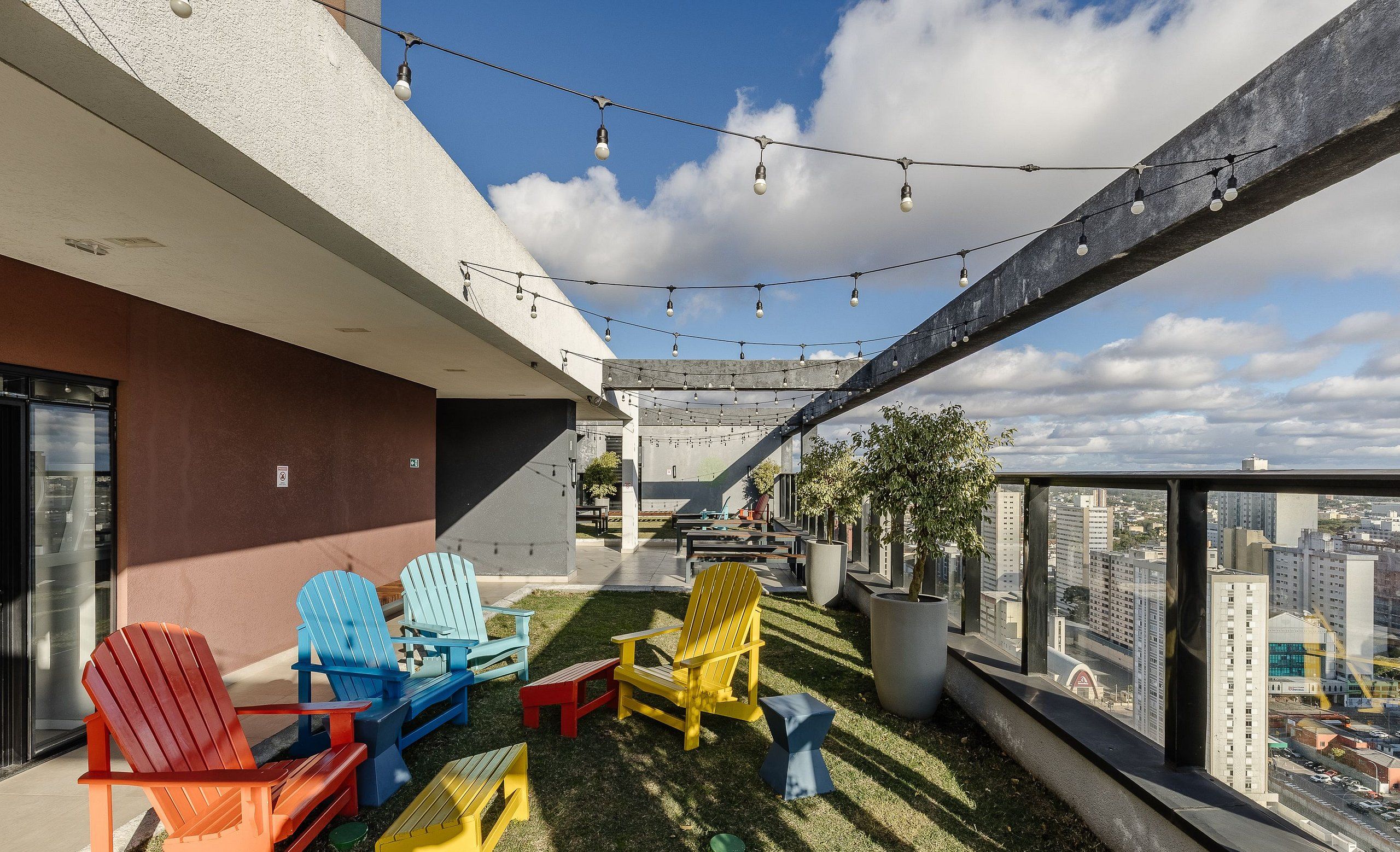 A rooftop patio with colorful Adirondack chairs, string lights, and a city view.