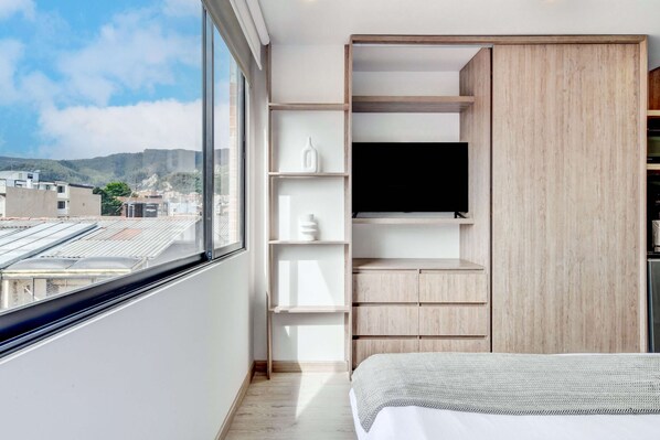 A modern bedroom with a large window, built-in shelving, and a flat-screen TV.