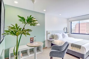 A modern hotel room with a bed, bedside table, chair, and a large plant. - Premium Loft in Bogota (Bogotá)