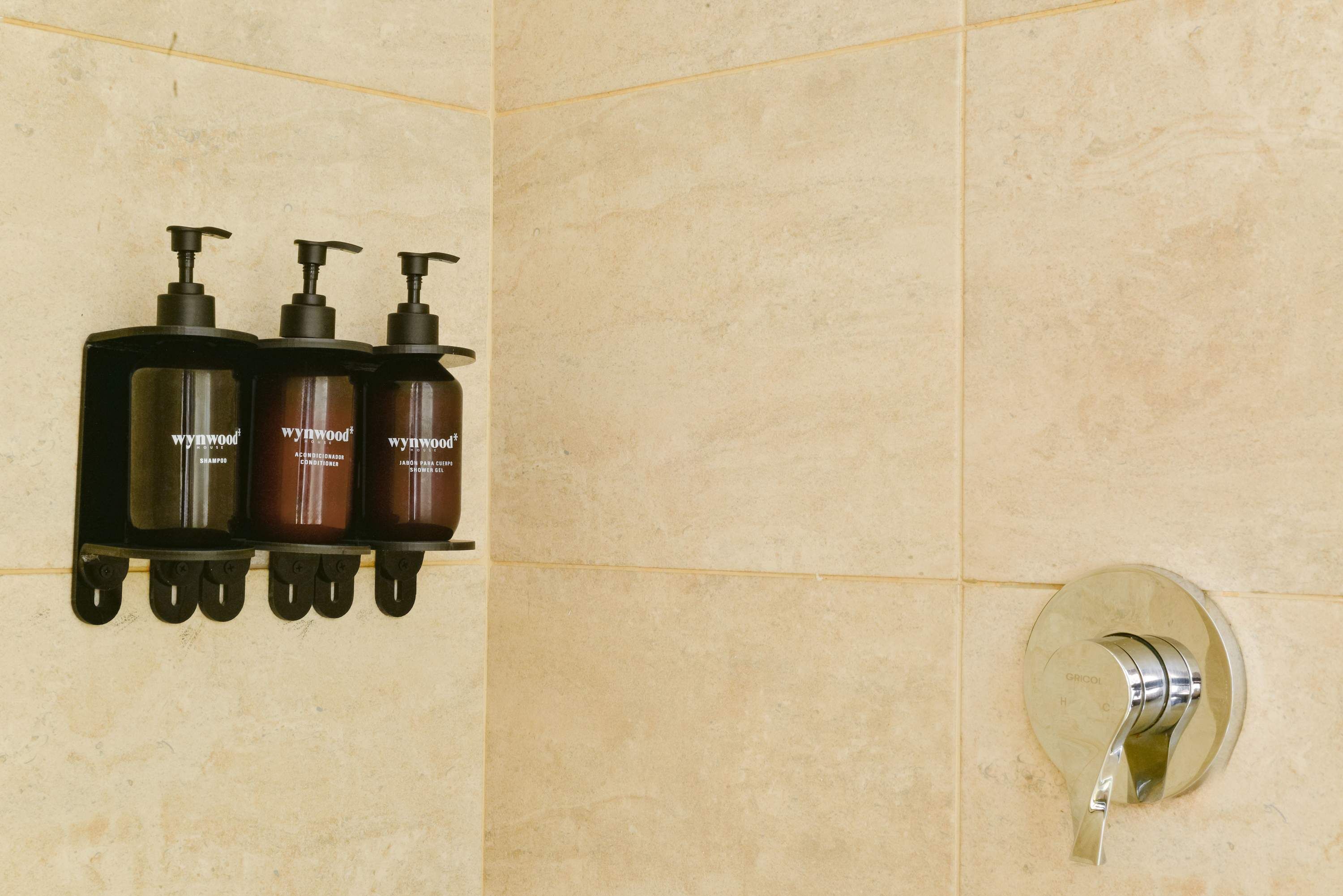 Een badkamer met drie flessen Wynwood shampoo op een zwart schap en een chromen doucheknop.