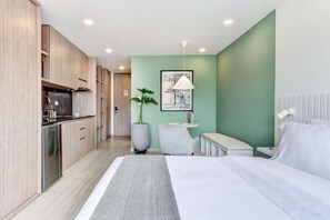 A modern hotel room with a bed, a small desk, a chair, a potted plant, and a kitchenette. - Premium Loft in Bogota (Bogotá)