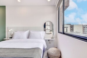 A modern hotel room with a large bed, a bedside lamp, a round mirror, and a view of the city through a large window. - Premium Loft in Bogota (Bogotá)