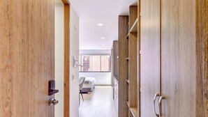 A hallway with wooden doors, a bed, and a window with a view of buildings.