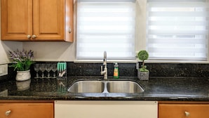 A kitchen with wooden cabinets, a double sink, a potted plant, and a window with blinds.