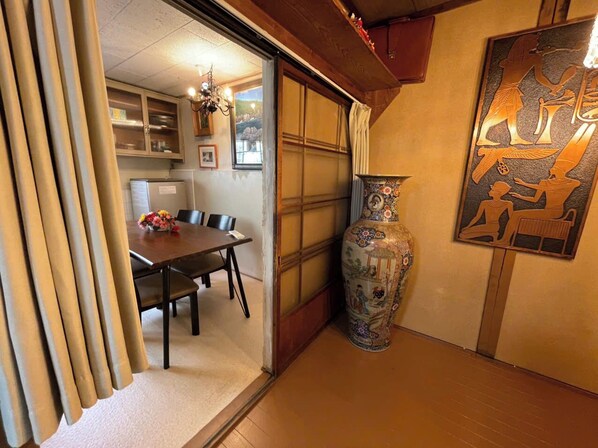A traditional Japanese room with tatami flooring, a low table with chairs, a large decorative vase, and a framed artwork on the wall.