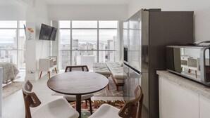 A modern apartment with a dining area, kitchen, and a large window offering a city view. - Studio cond c/ piscina 180m Hard Rock café ESR1912 (Curitiba)