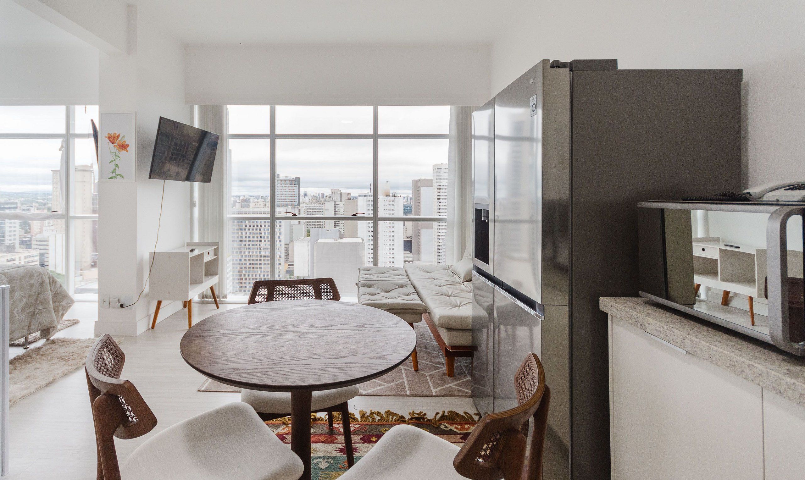 A modern apartment with a dining area, kitchen, and a large window offering a city view.
