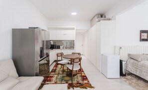 Een compacte leefruimte met een kitchenette, een eethoek met een gekleurd tapijt en een bed met hoofdeinde.