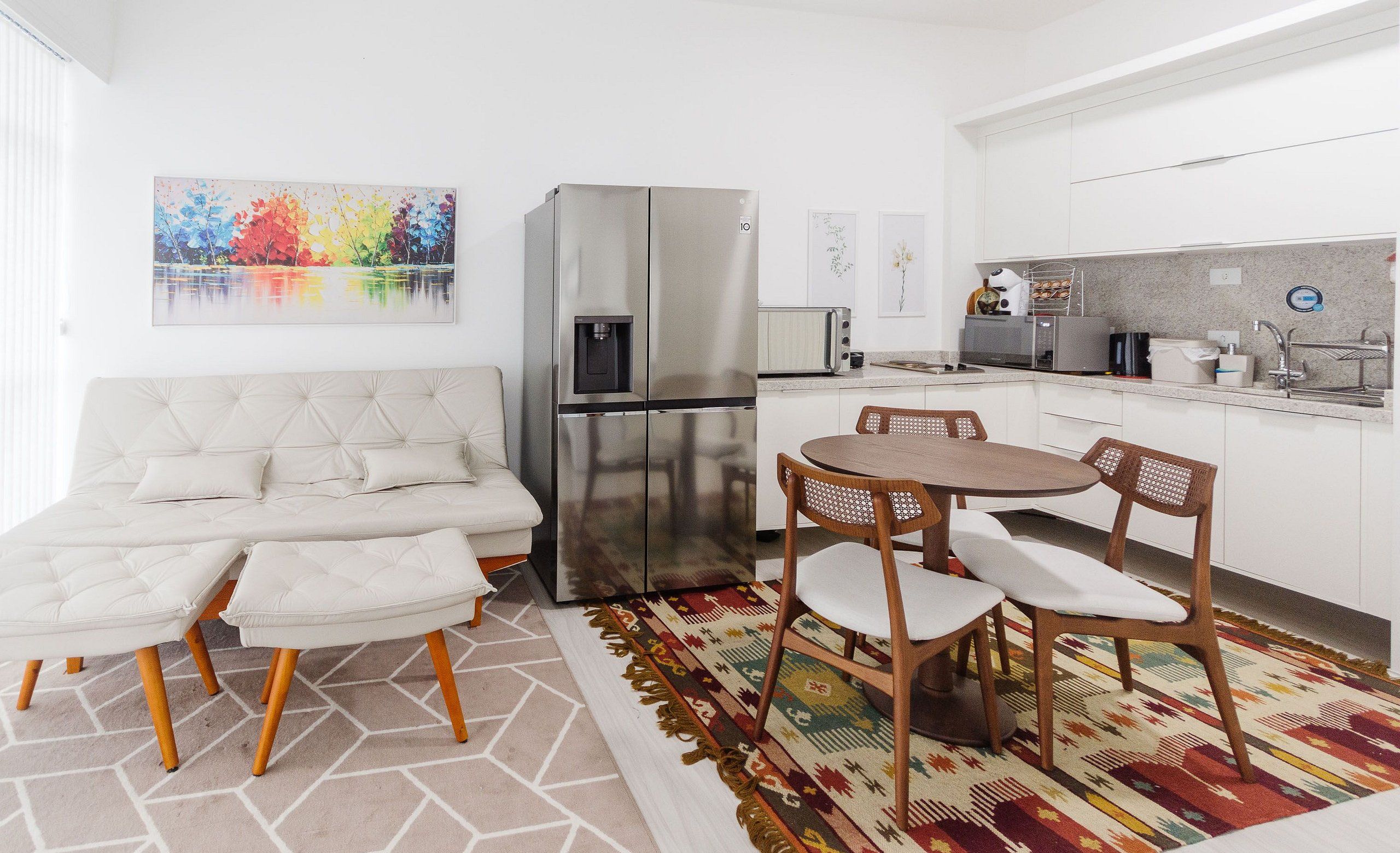 A modern kitchen with a refrigerator, microwave, and sink. There is a dining area with a table and chairs.