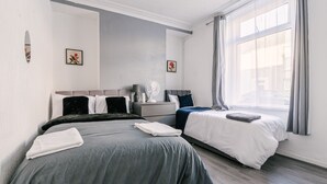 Een moderne hotelkamer met twee bedden, een nachtkastje met lamp en een groot raam met gordijnen.