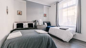 A modern hotel room with two beds, a bedside table with a lamp, and a large window with curtains.