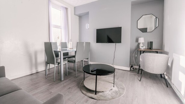 Een moderne woonkamer met een eethoek, een flatscreen televisie, een ronde salontafel en een zithoek.