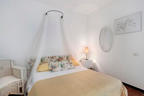 A bedroom with a bed, a chair, a bedside table with a lamp, and a wall-mounted mirror.