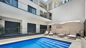 A modern indoor swimming pool with clear blue water, surrounded by white lounge chairs and umbrellas.