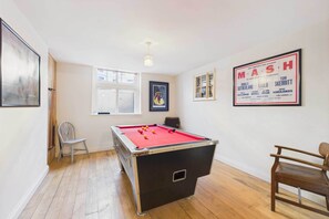 A room with a pool table, a chair, a framed poster on the wall, and a window.
