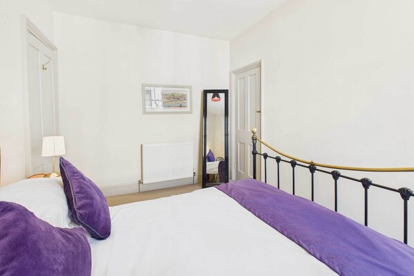 A bedroom with a bed, a nightstand, a lamp, a window, and a door.
