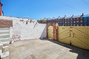 A courtyard with a white brick wall, a yellow gate, and a row of brick buildings in the background.