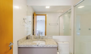 A modern bathroom with a marble sink, a glass shower enclosure, and a toilet.
